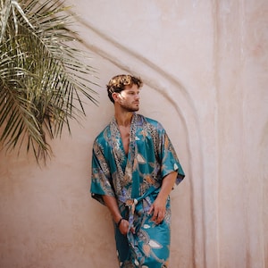 May include: A person wearing a teal blue silk robe with a colorful floral and geometric pattern. The robe has a sash tie at the waist.