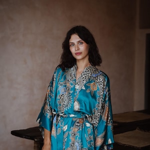 Puede incluir: Una bata de seda azul turquesa con un patr&oacute;n floral y geom&eacute;trico. La bata tiene un cintur&oacute;n de atar y mangas largas.