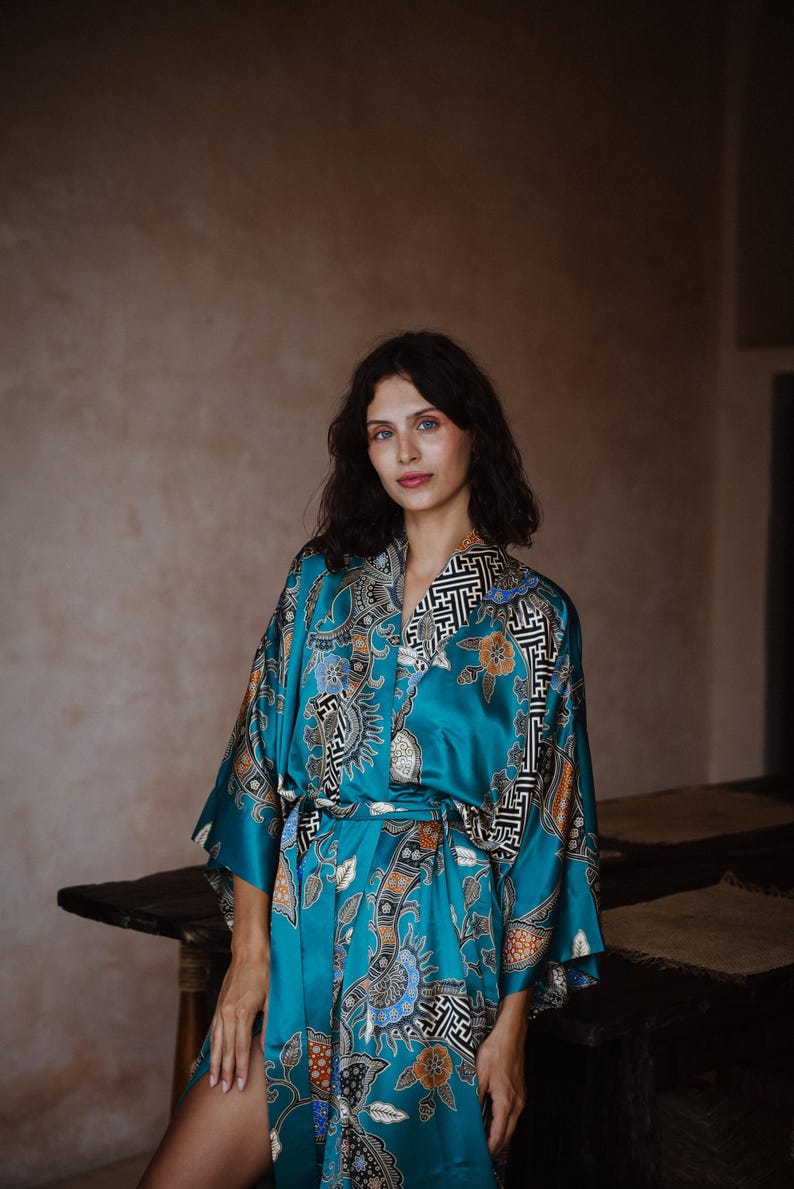 Puede incluir: Una bata de seda azul turquesa con un patr&oacute;n floral y geom&eacute;trico. La bata tiene un cintur&oacute;n de atar y mangas largas.