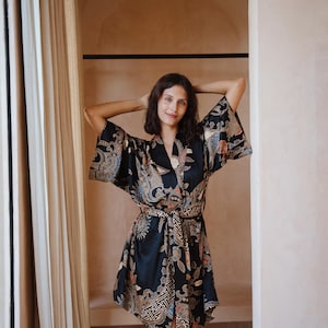 May include: A black silk robe with a colorful floral pattern and a matching sash. The robe has a kimono style with wide sleeves and a wrap closure.