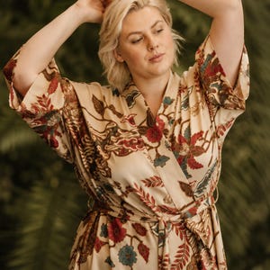 Könnte beinhalten: Ein beigefarbener Morgenmantel im Kimono-Stil mit einem detaillierten Blumen- und Blattmuster in Rot-, Dunkelbraun- und gedeckten Blautönen. Das Kleidungsstück hat weite Dreiviertelärmel, ein Wickeldesign mit Bindegürtel und einen V-Ausschnitt.