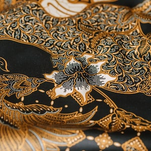 May include: Black fabric with a gold and white floral pattern. The fabric has a traditional Indonesian batik design.
