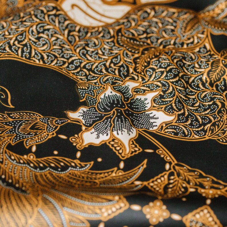 May include: Black fabric with a gold and white floral pattern. The fabric has a traditional Indonesian batik design.