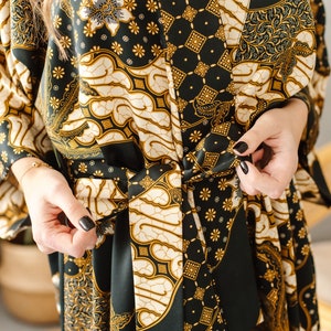 May include: A black and gold patterned silk robe with a tie belt. The robe has a traditional Indonesian batik design.