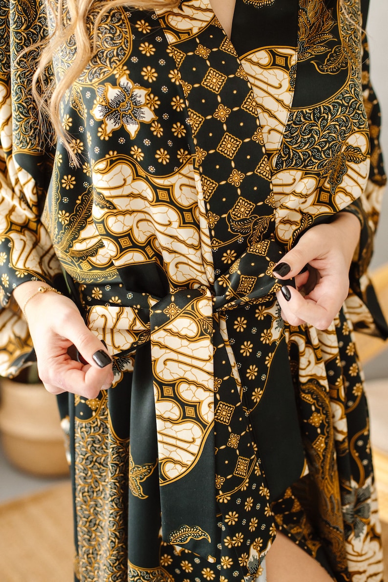 May include: A black and gold patterned silk robe with a tie belt. The robe has a traditional Indonesian batik design.
