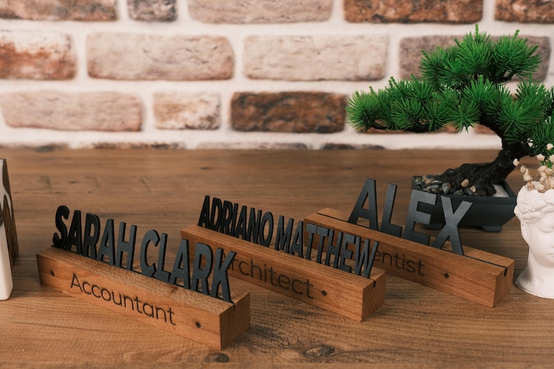 May include: Three wooden desk nameplates with black lettering. The nameplates read "Sarah Clark Accountant", "Adriano Matthew Architect", and "Alex Dentist".