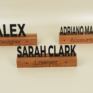 May include: Three wooden desk nameplates with black lettering. The top nameplate reads "ALEX Designer". The middle nameplate reads "SARAH CLARK Lawyer". The bottom nameplate reads "ADRIANO MATTHEW Accountant".