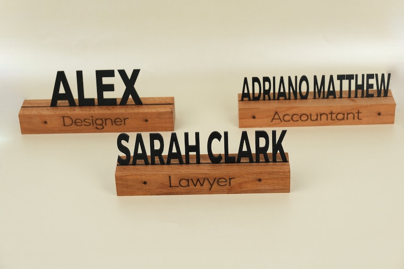 May include: Three wooden desk nameplates with black lettering. The top nameplate reads "ALEX Designer". The middle nameplate reads "SARAH CLARK Lawyer". The bottom nameplate reads "ADRIANO MATTHEW Accountant".