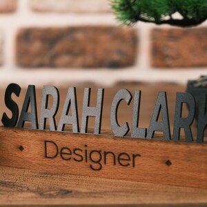 May include: A wooden desk nameplate with the name "SARAH CLARK" in black letters and the title "Designer" engraved below.