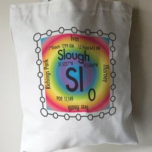 May include: White tote bag with a colourful graphic design featuring the word "Slough" and the text "SI 0" in a black circle. The graphic also includes the coordinates "51.5227°N 0.5164°W" and the text "POP. 11,149".
