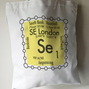 May include: A yellow tote bag with a black and white graphic of a London neighbourhood map. The map shows the area of SE London with the text "SE London" and the coordinates "51.4982°N 0.09031°W". The map also includes the names of surrounding neighbourhoods: South Bank, Vauxhall, Bankside, Southwark, and Bermondsey. The graphic also includes the text "Se 1" and "POP. 66,968".