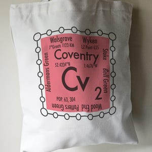 May include: A pink and white tote bag with a black outline and a graphic of a city map with the text "Coventry" and "Cv" in black. The map includes the coordinates 52.4234°N and 1.4676°W and the population 63, 304.