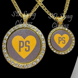 May include: Two gold chains with pendants featuring a grey heart with the initials "PS" in yellow on a sparkly background. The pendants are surrounded by a circle of clear rhinestones.