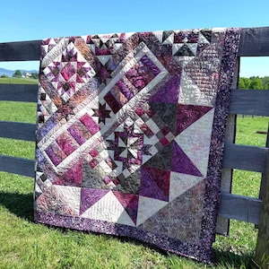 May include: A patchwork quilt featuring a complex geometric design with star and block patterns in shades of deep purple, magenta, black, and cream. The fabric displays varied textures and floral prints, finished with a dark purple floral border.