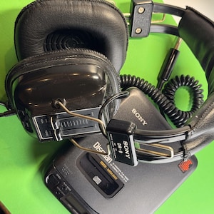 Pu&ograve; includere: Un lettore CD portatile Sony Discman nero con cuffie Sony DR-9 nere e un cavo a spirale. Il Discman ha una faccia argentata con il testo "Discman" e "SONY" stampato su di esso. Le cuffie hanno una manopola del volume e una manopola del tono.