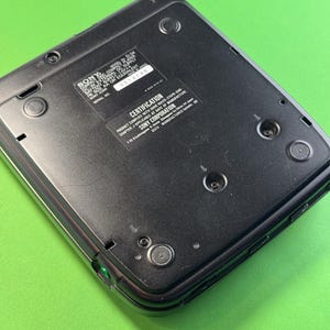 Pu&ograve; includere: Lettore CD Sony nero con un bordo argentato. La parte posteriore del lettore mostra il numero di modello, il numero di serie e le informazioni di certificazione. Il testo recita "SONY COMPACT DISC MODEL NO. D-34, EXT. DC SUPPLY 3V SIZE AA OR EQUIVALENT SONY CORP SERIAL NO. 3514146 CERTIFICATION PRODUCT COMPLIES WITH DANS LES-2107-2009- CHAPTER J-APPLICABLE AT DATE OF MANUFACTURE SONY CORPORATION 7-28 Kitasimachi, Minami-ku, Osaka 542-8511 JAPAN MANUFACTURED UNDER LICENSE",
