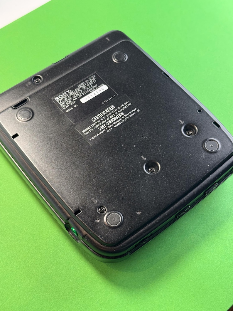 Pu&ograve; includere: Lettore CD Sony nero con un bordo argentato. La parte posteriore del lettore mostra il numero di modello, il numero di serie e le informazioni di certificazione. Il testo recita "SONY COMPACT DISC MODEL NO. D-34, EXT. DC SUPPLY 3V SIZE AA OR EQUIVALENT SONY CORP SERIAL NO. 3514146 CERTIFICATION PRODUCT COMPLIES WITH DANS LES-2107-2009- CHAPTER J-APPLICABLE AT DATE OF MANUFACTURE SONY CORPORATION 7-28 Kitasimachi, Minami-ku, Osaka 542-8511 JAPAN MANUFACTURED UNDER LICENSE",