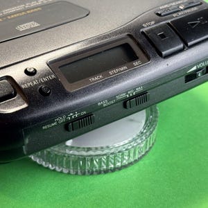 Pu&ograve; includere: Un lettore CD nero con una faccia argentata e una variet&agrave; di pulsanti, tra cui play, pausa, stop, ripetizione, traccia, passo/min, sec, hold, ripresa off, boost dei bassi, norm, mid, max e volume. Il lettore &egrave; posizionato su una superficie di vetro trasparente.