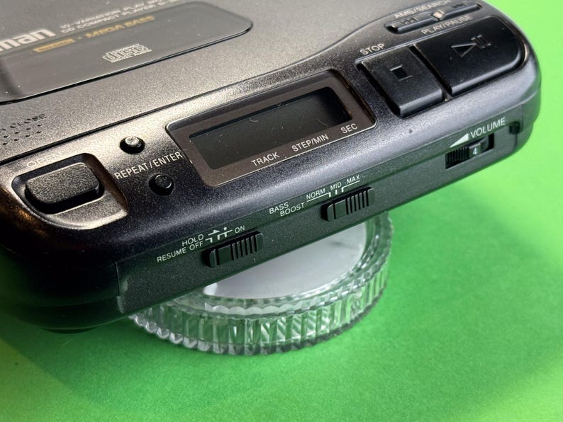 Pu&ograve; includere: Un lettore CD nero con una faccia argentata e una variet&agrave; di pulsanti, tra cui play, pausa, stop, ripetizione, traccia, passo/min, sec, hold, ripresa off, boost dei bassi, norm, mid, max e volume. Il lettore &egrave; posizionato su una superficie di vetro trasparente.