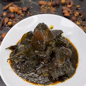 Könnte beinhalten: Eine weiße Schüssel gefüllt mit einem dunkelgrünen Eintopf mit Fleischstücken. Der Eintopf ist mit ein paar grünen Blättern garniert. Die Schüssel steht auf einer dunklen Oberfläche.