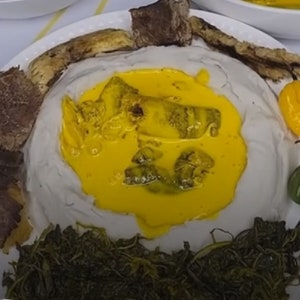 Könnte beinhalten: Ein weißer Teller mit einem Hügel aus weißem Essen, der mit einer gelben Sauce und grünem Gemüse bedeckt ist. Um den Hügel aus Essen herum befinden sich braune Fleischstücke und gelbe Paprika.