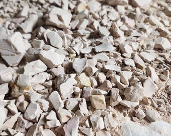 Könnte beinhalten: Ein Haufen unregelmäßig geformter, cremefarbener Steine und Fragmente. Die Steine sind unterschiedlich groß und haben eine leicht raue Textur. Der Hintergrund ist hellbraun und erzeugt eine natürliche, erdige Ästhetik. Das Bild deutet auf Rohmaterialien hin.