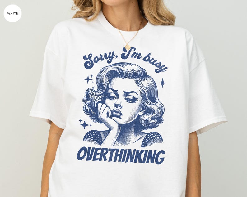 May include: White t-shirt with a blue graphic of a woman with the text "Sorry, I'm busy OVERTHINKING". The illustration features a vintage style with stars and a thoughtful pose.