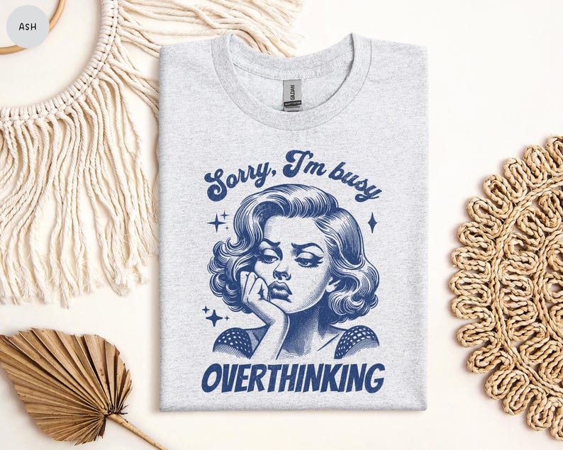 May include: Ash gray t-shirt with a blue graphic of a woman with the text "Sorry, I'm busy OVERTHINKING". The illustration features a vintage style with a woman resting her chin on her hand.