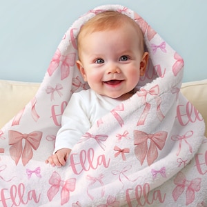 Pode incluir: Um beb&ecirc; envolto em um cobertor com capuz branco com um padr&atilde;o de la&ccedil;os rosa e o nome "Ella" em escrita rosa. O cobertor tem uma textura macia e felpuda e &eacute; drapeado sobre a cabe&ccedil;a do beb&ecirc;.