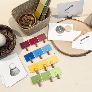 May include: A collection of educational materials including two woven baskets, a wooden slice, small wooden clothespins, paint color sample strips, and several white cards featuring illustrations of objects like a spoon, button, and honey dipper.