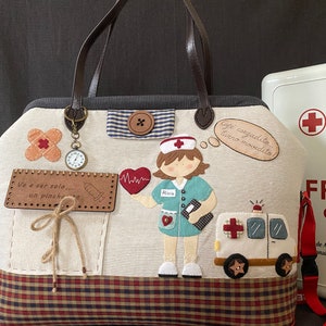 Puede incluir: Una bolsa de tela beige con fondo de cuadros rojos y negros. La bolsa tiene varios apliques, incluyendo una enfermera de dibujos animados, un corazón, una venda, una jeringa, un reloj y una pequeña ambulancia. La bolsa tiene un asa de cuero marrón y una correa roja. El texto en la bolsa dice "Café cargadito... turno movidito" y "Ve a ser solo... un pinche".