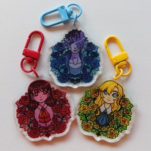 Può includere: Quattro portachiavi in acrilico con disegni di personaggi dei cartoni animati, ciascuno circondato da una ghirlanda floreale. I portachiavi presentano un personaggio dai capelli rossi, un personaggio con i capelli viola e un personaggio biondo. Ogni portachiavi ha un fermaglio di colore diverso.