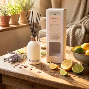 May include: A white reed diffuser with black reeds and a copper-colored collar, labeled "SCENT GROVE Lemon & Lime." The product is displayed with a box, lemons, limes, and lavender on a wooden table. The diffuser is a home fragrance product.