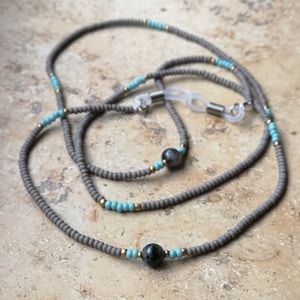 Könnte beinhalten: Graue Perlenkette für Brillen mit türkisfarbenen und goldenen Perlen und zwei schwarzen Edelstein-Akzenten.