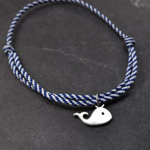 Könnte beinhalten: Ein weiß-blaues, gestreiftes Seil-Armband mit einem silbernen Wal-Anhänger.