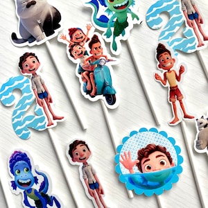 May include: A set of 10 cupcake toppers featuring characters from the animated film Luca. The toppers include Luca, Alberto, Giulia, a sea monster, a cat, and the number 2. The toppers are printed on white cardstock and have a blue and white color scheme.