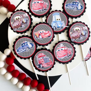 Puede incluir: Un conjunto de 10 adornos para cupcakes con personajes de la pel&iacute;cula Cars. Los adornos est&aacute;n impresos en c&iacute;rculos redondos y festoneados con un patr&oacute;n de cuadros negros y blancos. Los personajes incluyen Rayo McQueen, Mate, Mate el remolque, y m&aacute;s.