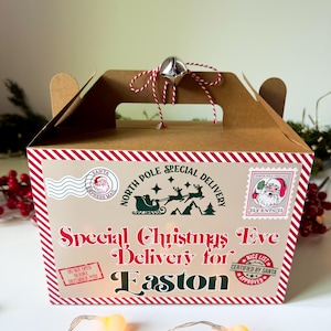 May include: A brown cardboard gift box with a red and white striped border. The box is labeled "Special Christmas Eve Delivery for Easton" with festive graphics and a silver bell on top. Includes postage stamps.