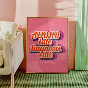 Puede incluir: Un póster rosa enmarcado con las palabras "AUDHD late diagnosis club" en una fuente retro. El texto tiene un contorno blanco y una sombra azul. El póster está en un marco dorado y está colocado contra una pared rosa.