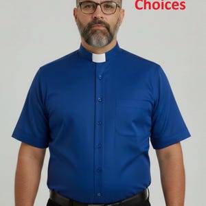 May include: A short-sleeved royal blue clergy shirt featuring a white clerical collar insert, a front button placket, and a single chest pocket. The text 13 Colour Choices is visible in the upper right corner of the image.
