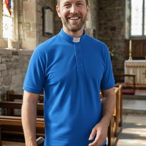 Op de afbeelding: Een felblauw overhemd met korte mouwen voor geestelijken, voorzien van een opstaande kraag met een wit inzetstuk en een gedeeltelijke knoopsluiting aan de voorzijde. Het overhemd is gemaakt van effen stof en gecombineerd met een zwarte broek.