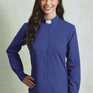 May include: A long-sleeved royal blue clergy shirt featuring a button-down front placket and a white clerical collar insert. The shirt has a structured collar, long sleeves with buttoned cuffs, and a straight hemline, providing a formal appearance.