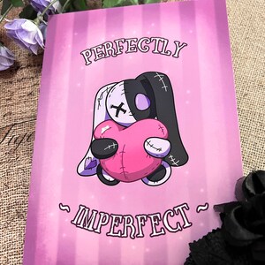 May include: A pink and purple print with a stitched cartoon bunny holding a pink heart. The text reads "Perfectly Imperfect".