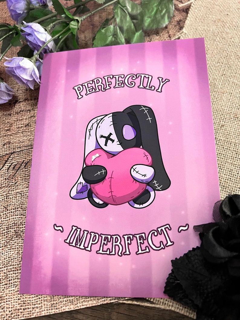 May include: A pink and purple print with a stitched cartoon bunny holding a pink heart. The text reads "Perfectly Imperfect".