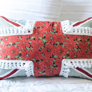 May include: A green and white pillow with red poinsettia print and white fringe trim. The pillow has a red and white stripe on each side.