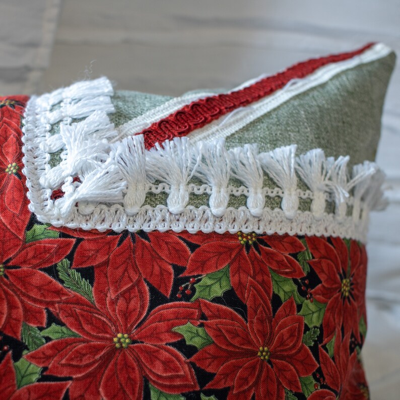 May include: A green and white pillow with a red trim and white fringe. The pillow has a red poinsettia print.