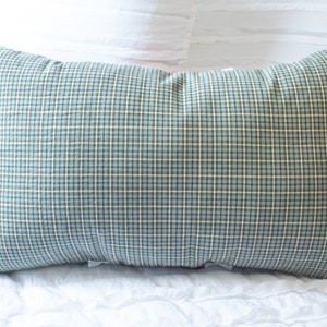 May include: A blue and white plaid pillow with a soft, textured fabric. The pillow is lying on a white bedspread.