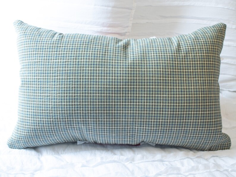 May include: A blue and white plaid pillow with a soft, textured fabric. The pillow is lying on a white bedspread.