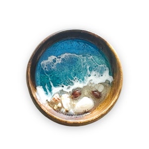 May include: A wooden bowl with a blue and white resin ocean scene and seashells. The resin is clear and shows the shells embedded in the resin.