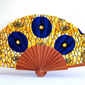 May include: A folding hand fan featuring a vibrant yellow fabric canopy with a black net-like pattern and large, circular blue and yellow floral motifs. The fan is supported by a brown wooden frame with thin, radiating slats and a central pivot.
